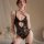 Woman modeling black yue die sexy lace bodysuit with open-crotch design, sheer floral lace, and elegant jewelry.